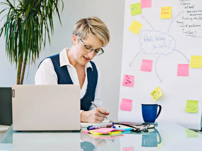 An image of Bryony reading some work at a desk, with a flip chart from a workshop behind