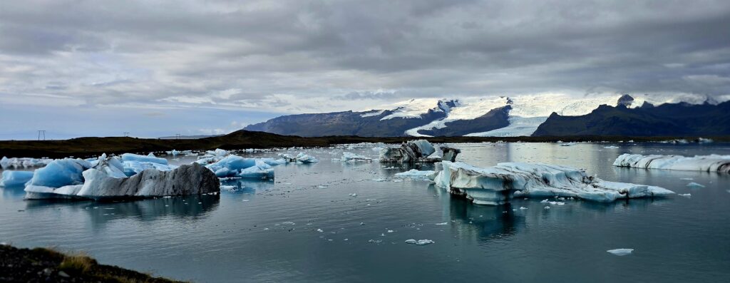 Glaciers of blue ad white floating on the Jokursarlon Glacier Lagoon. In the background are glaciers creeping down to the lagoon from the black mountains.