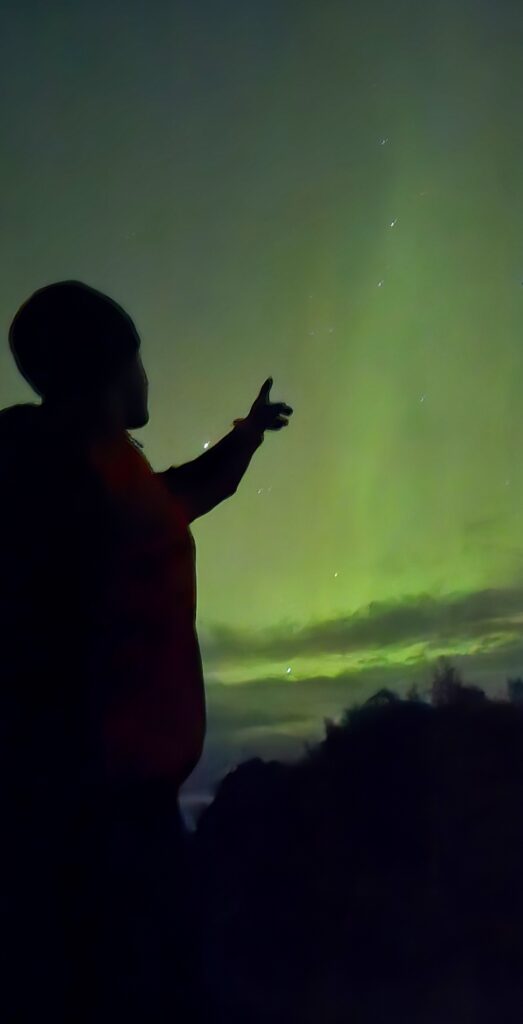 A silhouette of my son pointing to the green skies, looking at the Northern Lights