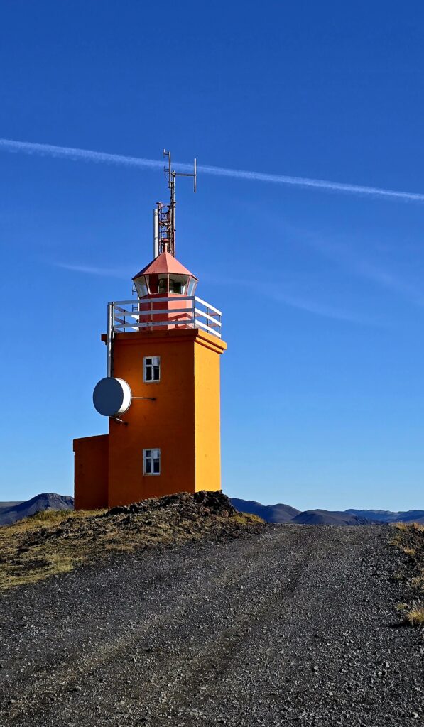 Hópsnes Lighthouse, very near Grindavik. A bright orange lighthouse with a blue sky backdrop.