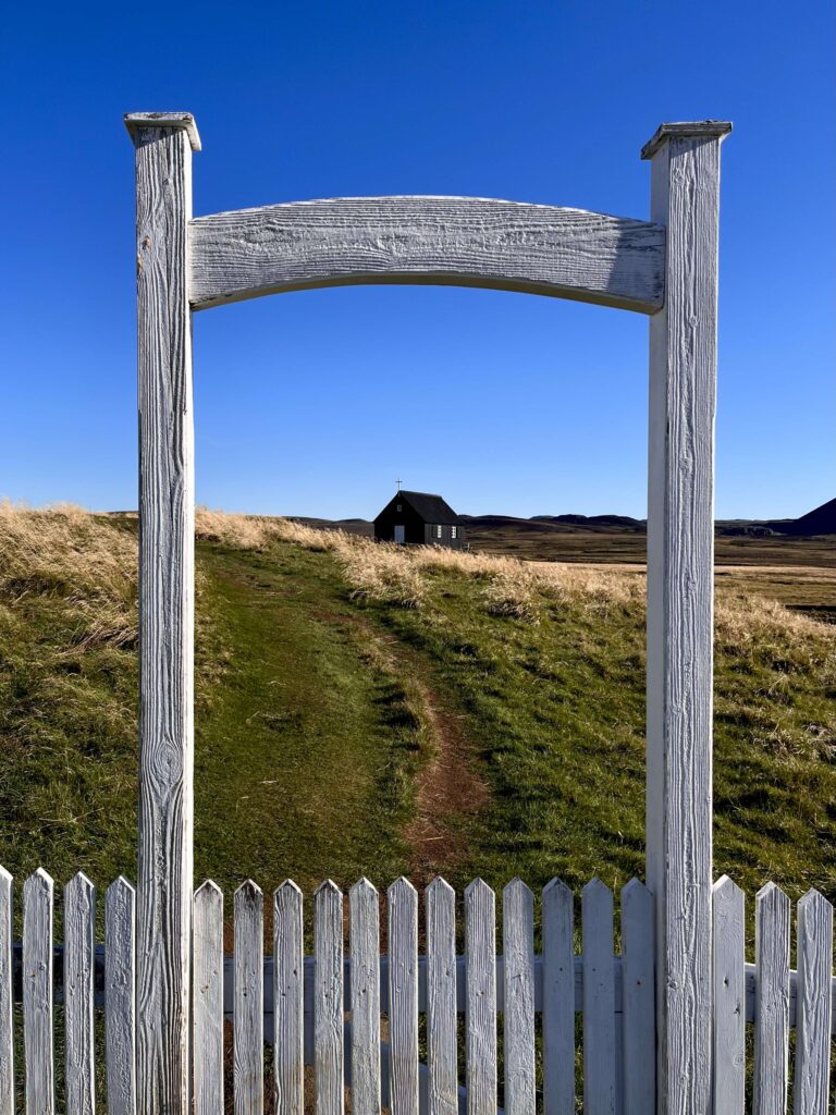 Image of the small black church Krysuvikurkirkja framed by a white entrance arch with a blue sky.