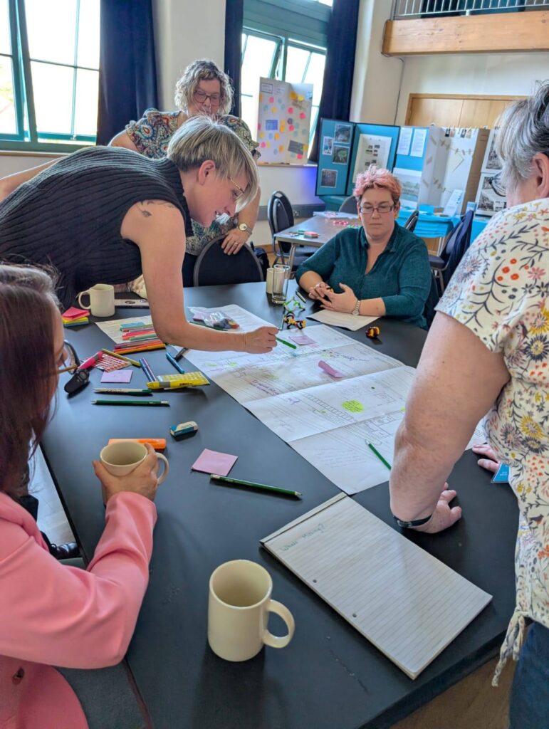 Image of group discussion with Bryony looking at architect drawings and talking with the working group who are gathered around a table.